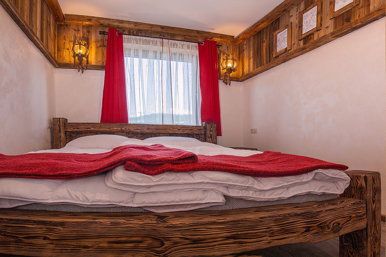 Wygodne drewniane łóżko z czerwoną narzutą w sypialni apartamentu Jaworczański Raj pod Wysoką