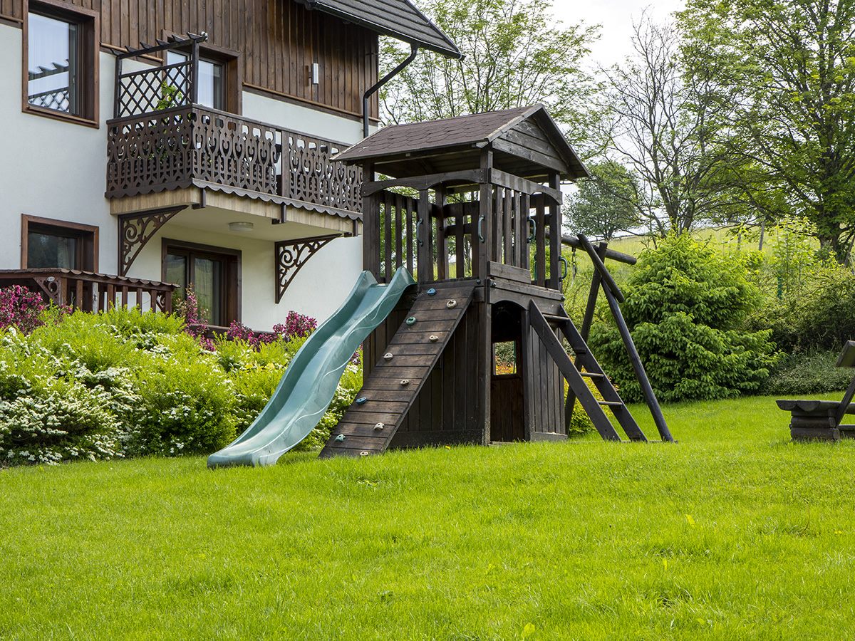 Zbliżenie na drewniany plac zabaw ze zjeżdżalnią i ścianką wspinaczkową w ogrodzie przy apartamentach
