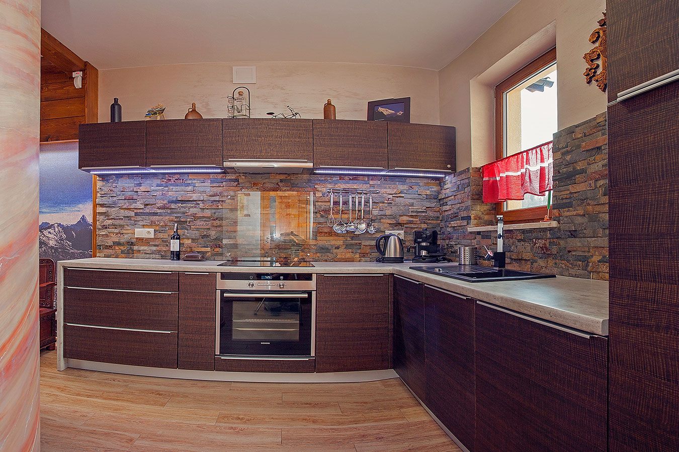 Elegancki aneks kuchenny w Apartamencie na Szczycie z ciemnymi drewnianymi szafkami, kamiennym wykończeniem ściany i subtelnym oświetleniem LED