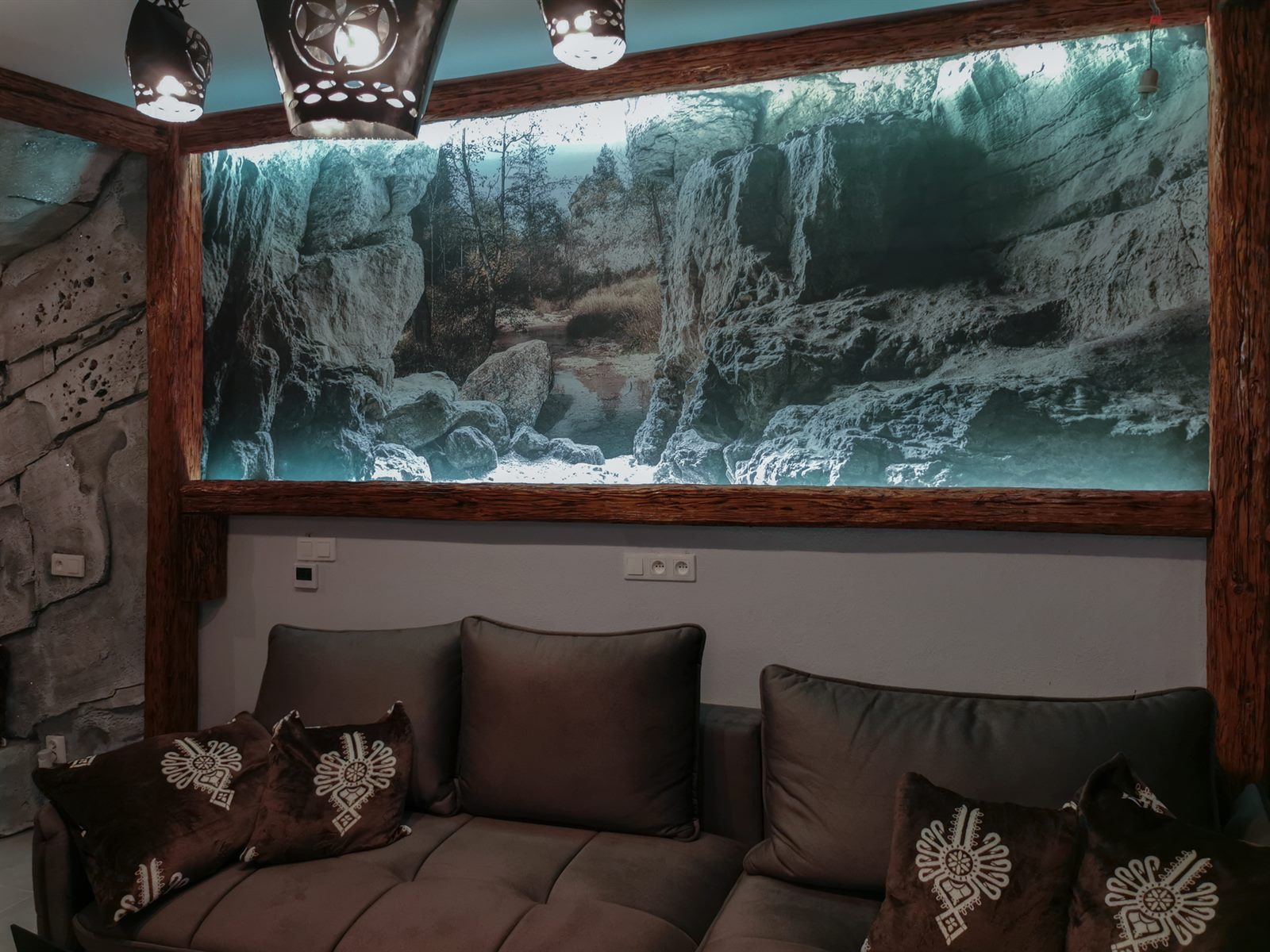 Wygodna sofa z ozdobnymi poduszkami na tle podświetlanej fototapety przedstawiającej górski skalny wąwóz