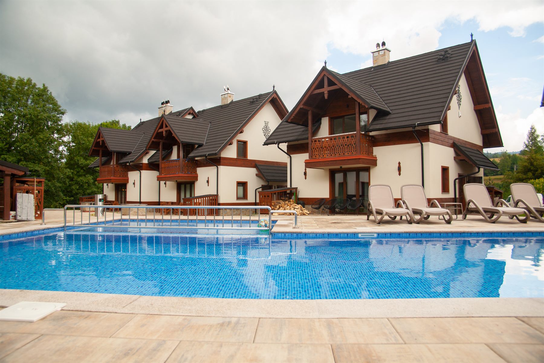 Widok z poziomu basenu na eleganckie budynki kompleksu apartamentów z charakterystycznymi drewnianymi zdobieniami